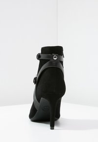 Zwarte suède enkellaars met een hoge stiletto hak. Bevat een glanzende zwarte riem met een decoratieve gesp aan de zijkant. Glad van textuur.
