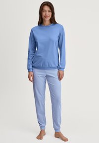 Hellblaues Langarmoberteil, kombiniert mit blau-weiß gestreiften Schlafanzughosen. Die Materialien wirken weich, mit einem lässigen Schnitt und elastischen Bündchen.