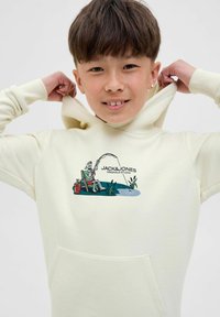 Hoodie crème clair avec une poche avant et un imprimé graphique représentant un squelette en train de pêcher. Fabriqué en tissu doux et texturé. Design lisse.