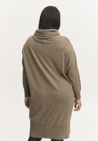 Robe pull surdimensionnée vert olive avec un col cheminée, des manches longues et des fentes latérales ; texture tricotée et coupe décontractée.