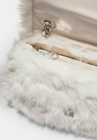 Bílá kabelka z umělé kožešiny se stříbrným řetízkem a béžovým koženým interiérem s přihrádkou na zip.
