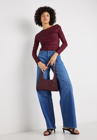 Burgundijas krāsas garām piedurknēm topiņš ar pieguļošu dizainu, apvienots ar platām ziliem džinsiem, turētājs ar mazu burgundijas krāsas rokassomu un melniem augstpapēžu sandaliem.