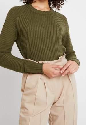 Pull en maille côtelée vert olive avec des manches longues et un col rond, assorti à un pantalon plissé beige taille haute. Texture lisse.