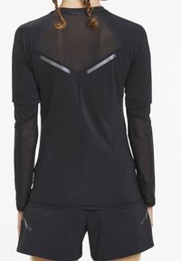 Maglietta sportiva nera con maniche lunghe trasparenti e pannello posteriore in rete. Presenta dettagli riflettenti e una silhouette aderente. Abbinata a pantaloni corti neri.