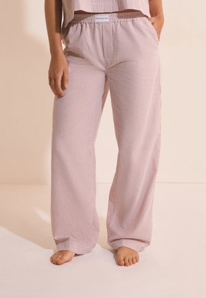 Pantalones sueltos a rayas rosas y blancos con cintura elástica y bolsillos, usados descalzos por una persona de pie sobre un fondo liso.