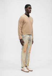 Suéter de punto beige, jeans claros desgastados con manchas naranjas y zapatillas beige con rayas texturizadas. Diseño simple y casual.