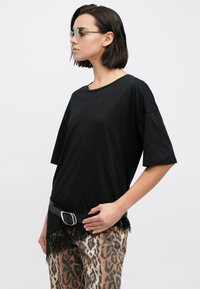 Černé oversize tričko s krátkými rukávy a kulatým výstřihem, kombinované s kalhotami s leopardím vzorem, které mají krajkový lem a černý pásek.