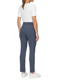 Pantalon bleu marine au design ajusté et jambes droites, fabriqué en tissu texturé, avec une poche arrière. Porte avec un haut blanc et des baskets.