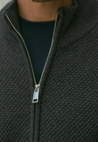 Ciemnoszara rozpinana bluza z teksturowanym wzorem, z metalowym suwakiem i t-shirtem z okrągłym dekoltem pod spodem.