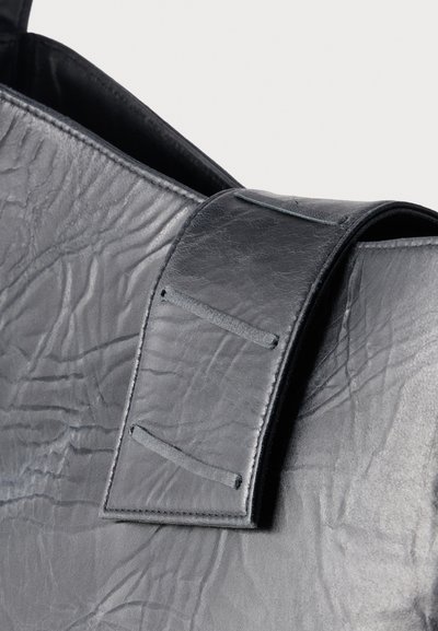 Κοντινό πλάνο μαύρης δερμάτινης τσάντας με υφή επιφάνειας και φαρδιά λουράκι ραμμένο με ορθογώνιες θηλιές.