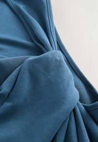 Modrý textilní top s uzlovým designem. Měkká textura s hladkým povrchem a jemným elastickým efektem. Viditelné švy podél okrajů.