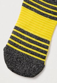 Κίτρινη και σκουρόγρια περιοχή στο δάχτυλο της κάλτσας με εναλλασσόμενες οριζόντιες ρίγες και ριμπ υφή σε λευκό φόντο.