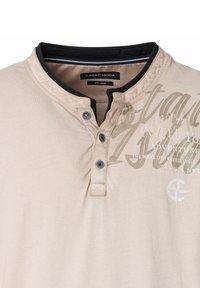 Lässiges beiges Polohemd mit einem schwarzen Kragen, zwei Knöpfen und einem bedruckten Textdesign auf der Vorderseite. Hergestellt aus einem weichen Stoff. Größe groß.