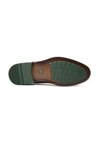 Brown and green rubber sole with a textured tread. Features a circular logo at the center and lines for grip on the sides.
