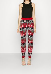 Leggings rouges et noirs avec un motif de vacances comprenant des flocons de neige, des arbres et des rennes. Taille élastique, design ajusté, tissu doux.