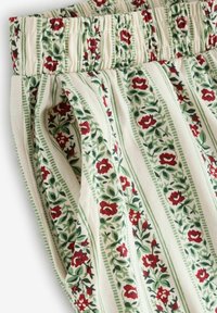 Auduma ar ziedu rakstu, kurā ir sarkanas rozes, zaļas lapas un vertikālas svītras uz krēmkrāsas fona. Redzams detalizēts elastīgās jostas vietas attēlojums.