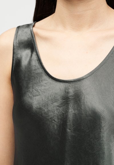 Κοντινό πλάνο ενός ατόμου που φοράει αμάνικο, σκούρο γκρι σατινέ τοπ με λαιμόκοψη σε σχήμα σχήματος scoop, που αφήνει ακάλυπτη την κλείδα και το άνω μέρος του στήθους.