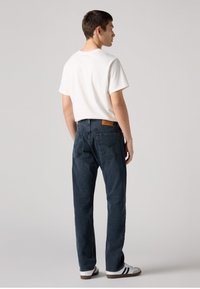Jeans azul escuro com um corte reto, em material de algodão, e bolsos traseiros. Combinados com uma t-shirt branca simples e ténis brancos.