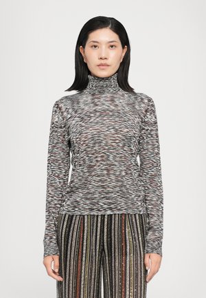 Top de cuello alto ajustado de manga larga en una tela texturada multicolor con un patrón ondulado; combinado con pantalones de pierna ancha a rayas y brillantes.