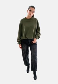 Olijfgroen oversized sweatshirt met lange mouwen, gecombineerd met hoog waisted donkerdenim jeans en zwarte enkellaarsjes. Eenvoudig en modern ontwerp.