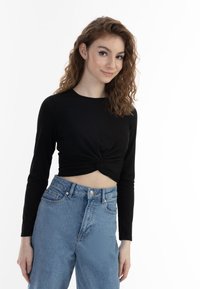 Top corto nero a maniche lunghe con dettaglio a torsione sul davanti, abbinato a jeans in denim azzurri a vita alta.