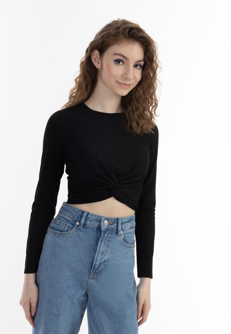 Černý dlouhý rukáv cropped top s kroucením v přední části, spárovaný s světle modrými džíny s vysokým pasem.