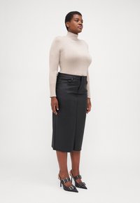 Gaisbeige turtlenecks džemperis, kombinēts ar melnu ādas midi svārku un melniem augstpapēžu apaviem ar sprādžu akcentiem.