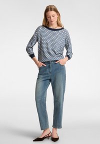 Maglietta a maniche lunghe blu con motivo e rifiniture blu navy, abbinata a jeans dritti blu chiaro e scarpe con tacco marroni.
