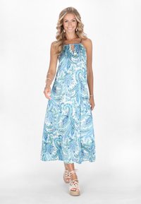 Rochie maxi albă și albastră cu imprimeu paisley, cu decolteu adunat și detaliu în formă de cheie. Croială lejeră, material fluid, asortată cu sandale cu platformă în culori deschise.