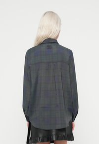 Tummanvihreä ja tummansininen ruudullinen pitkähihaisessa paidassa on kaulus, nappikäsivarat ja hienovarainen laskostus selkäpuolella lisäyksinä.