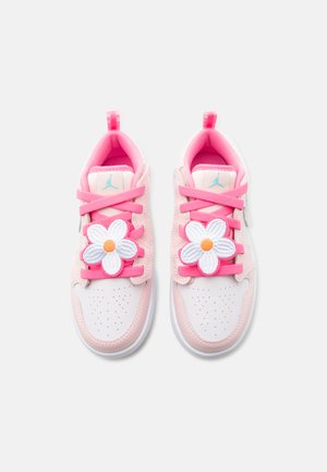 Rózsaszín és fehér tornacipő pár világos rózsaszín fűzőkkel és nagy fehér virág díszekkel a tetején, fehér háttér előtt.