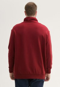 Czerwony polarowy sweter z wysokim kołnierzem, długimi rękawami i ściągaczami przy nadgarstkach. Charakteryzuje się gładką teksturą i luźnym krojem.