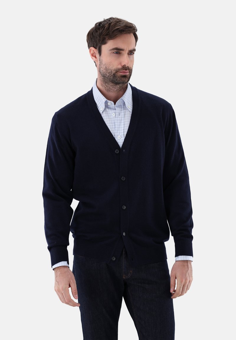 Marinefarbener Cardigan mit V-Ausschnitt, fünf Knöpfen, gerippten Bündchen und glatter Textur, getragen über einem hellen karierten Hemd.