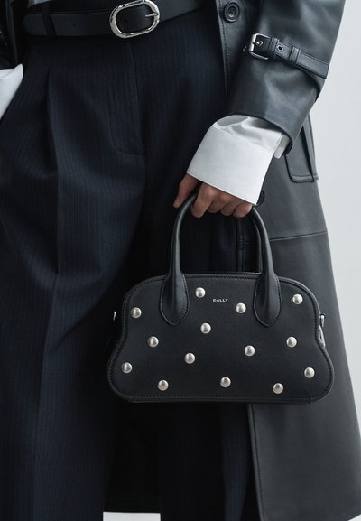 Black leather handbag with silver studs on the front, rounded shape, dual top handles, and a zip closure. Brand name "Bally" is visible.
