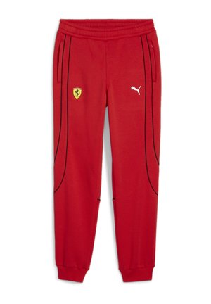 Enfant portant un t-shirt rouge aux marques Ferrari et Puma, un pantalon de jogging et des baskets rouges, debout devant un fond gris clair uni.