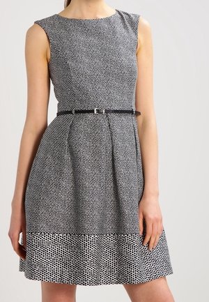 Sukienka bez rękawów w biało-czarne groszki, dopasowana w talii, z wąskim czarnym paskiem, o długości do połowy uda.