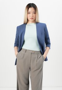Bordo modri blejzer s trečjinskimi ruffled rokavi, v kombinaciji s svetlo mentolasto zgornjo majico in sivimi hlačami z visokim pasom, ki imajo gumbni detajl.