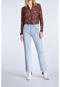 Chemise à manches longues florale dans des teintes rouges et sombres, associée à un jean taille haute bleu clair avec des détails déchirés, et des bottes à talons blanches.