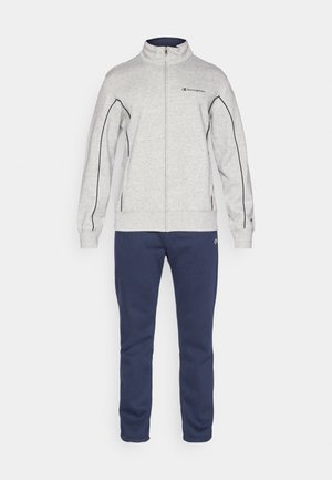 Hallhalli halli, millel on tumesinised aktsendid ja logo rinnal, koos tumesiniste dressipükstega, mis on valmistatud pehmest, struktureeritud kangast.