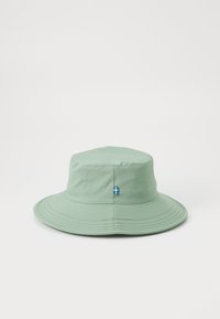 Svetlozelený klobúk typu bucket vyrobený z jemnej látky, s vyšitým logom a malou akcentovanou švédskou vlajkou na boku. Široký, šikmý okraj.