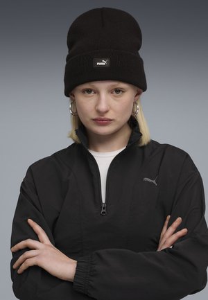 Czarna kurtka zapinana na zamek z białym kołnierzem, z małym szarym logo Pumy. W połączeniu z czapką beanie z dzianiny oraz dużymi srebrnymi kolczykami w kształcie kół.