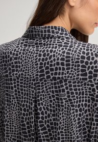 Langarmshirt met een zwart en grijs abstracte print, voorzien van een kraag en een subtiel logo op de achterkant. Zachte stof met een gladde textuur.