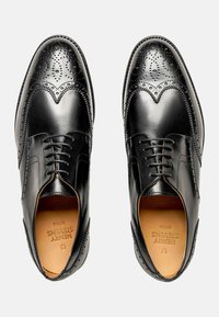 Chaussures habillées en cuir noir avec un design brogue, un bout pointu, des perforations complexes et un système de laçage. Fini classique et brillant.