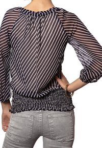 Blusa a righe blu navy e bianche con maniche lunghe, vita arricciata e tessuto trasparente. Presenta un colletto rotondo e un accento elastico all'orlo.