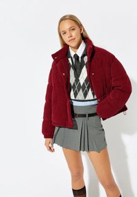 Burgunderfarbene Corduroy-Steppjacke, grauer Faltenrock, weißes Hemd mit Knöpfen, schwarze Krawatte, argyle Strickjacke; Texturiertes und geschichtetes Outfit.