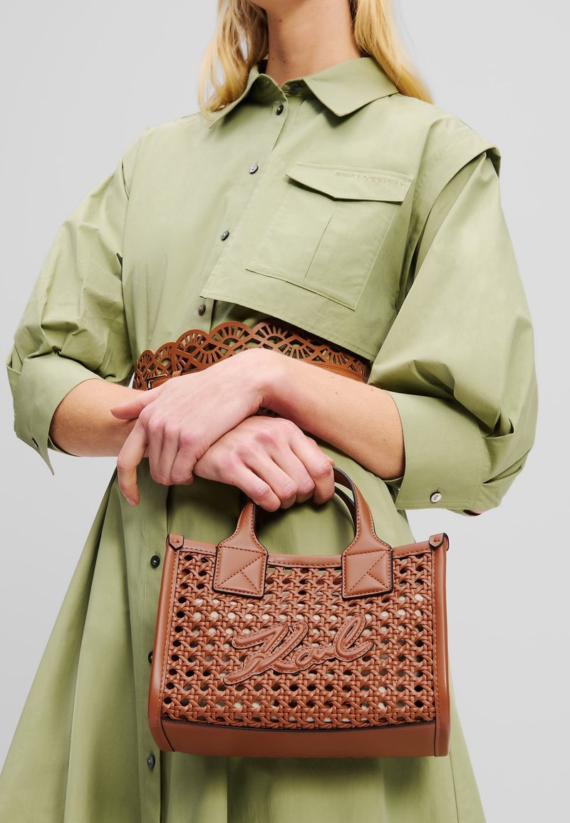 Femme en robe-chemise vert olive tenant un sac à main en cuir tressé marron avec "Karl" brodé sur le devant.