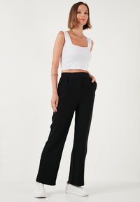 Zwarte wijde broek met voorplooien en zijzakken, gecombineerd met een nauwsluitende witte crop top. Gladde stof, strakke lijnen en een casual uitstraling.