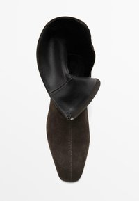 Bottine en suède marron avec un empiècement en cuir noir replié, bout pointu et coutures visibles le long de la semelle, dotée d'un intérieur lisse.