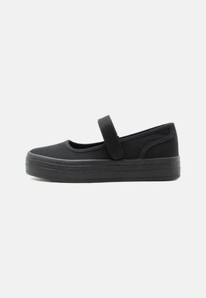 Chaussure Mary Jane noire avec semelle en caoutchouc épaisse et bride ajustable à fermeture Velcro, conçue pour un usage décontracté avec un bout arrondi.