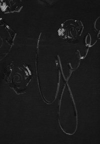 Tissu noir avec des motifs floraux embellis de sequins et un design de signature stylisé, créant une surface texturée et réfléchissante.